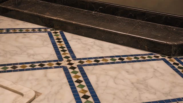 A veined marble floor inlaid with bands of blue zellige.