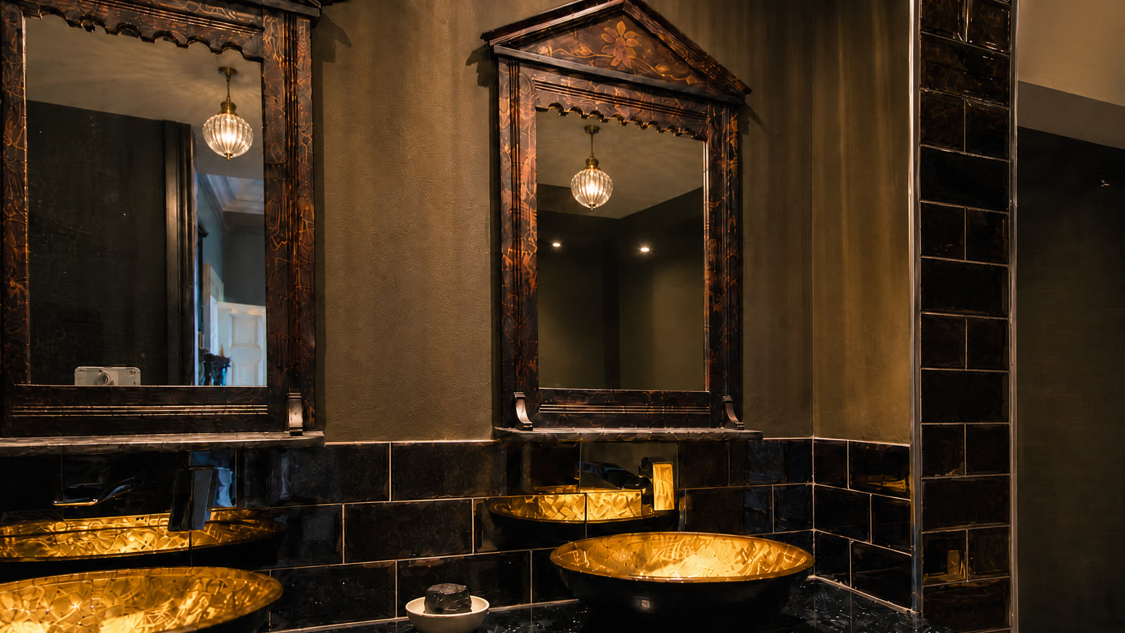 Hammered brass basins under carved-frame mirrors.