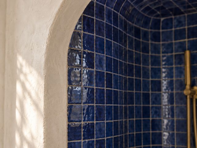 Arched shower niche lined with blue zellige in a plaster wall
