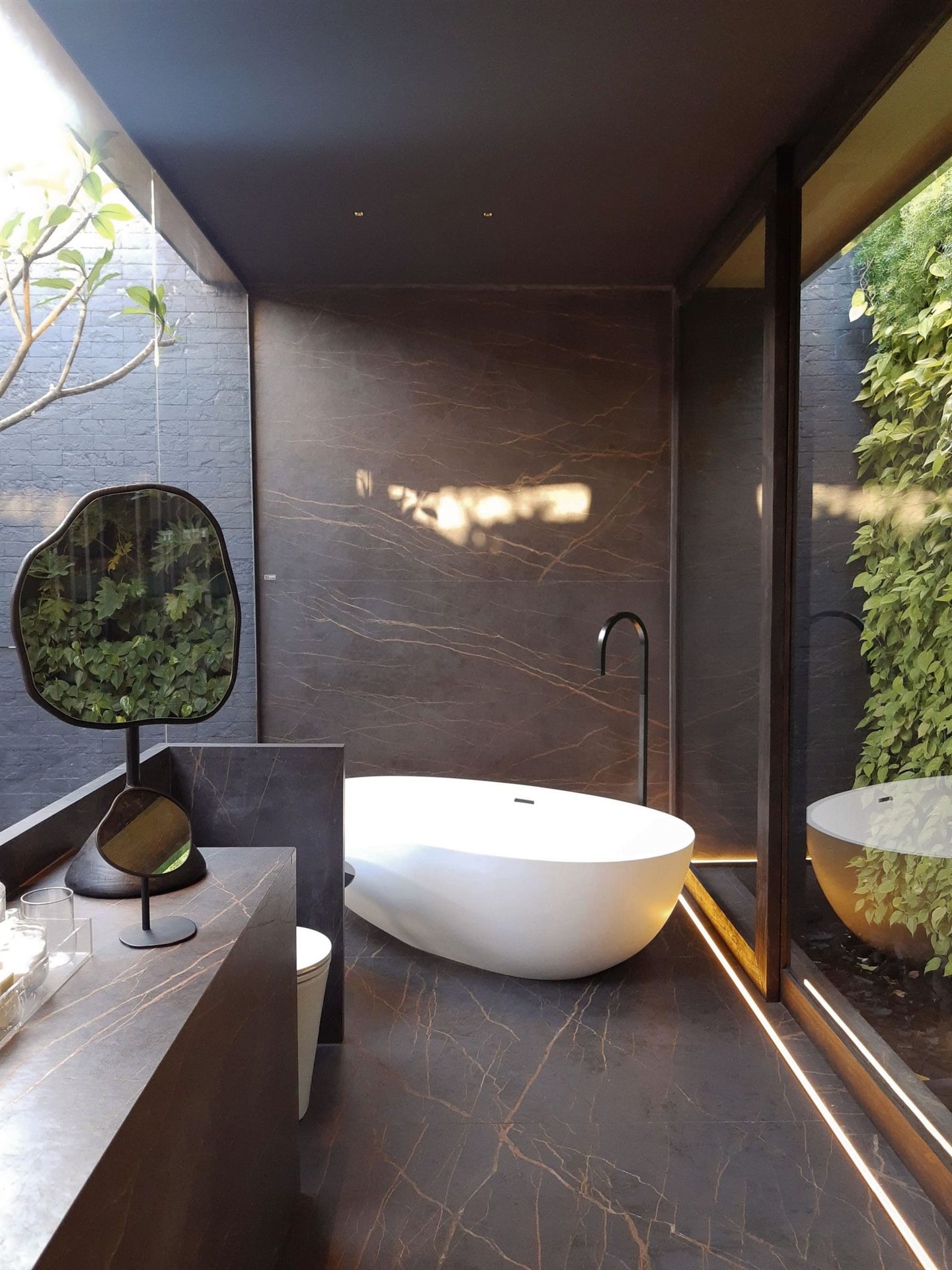 Salle de bain en marbre sombre avec baignoire îlot, ouverte sur un jardin vertical