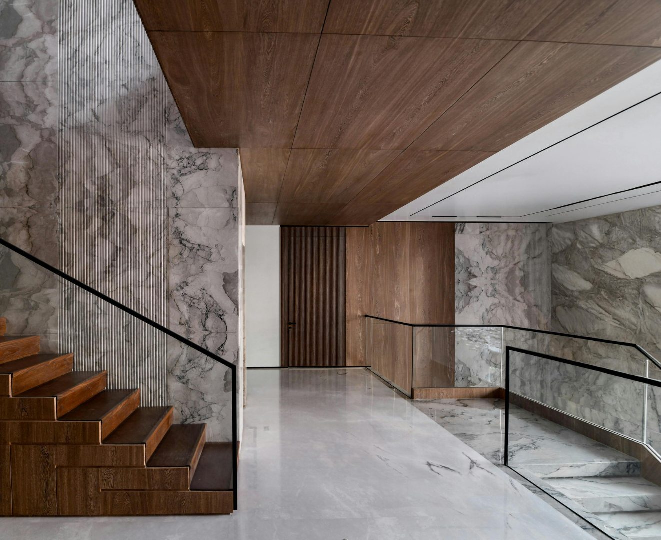 Escalier aux marches de bois, garde-corps de verre et murs de marbre clair