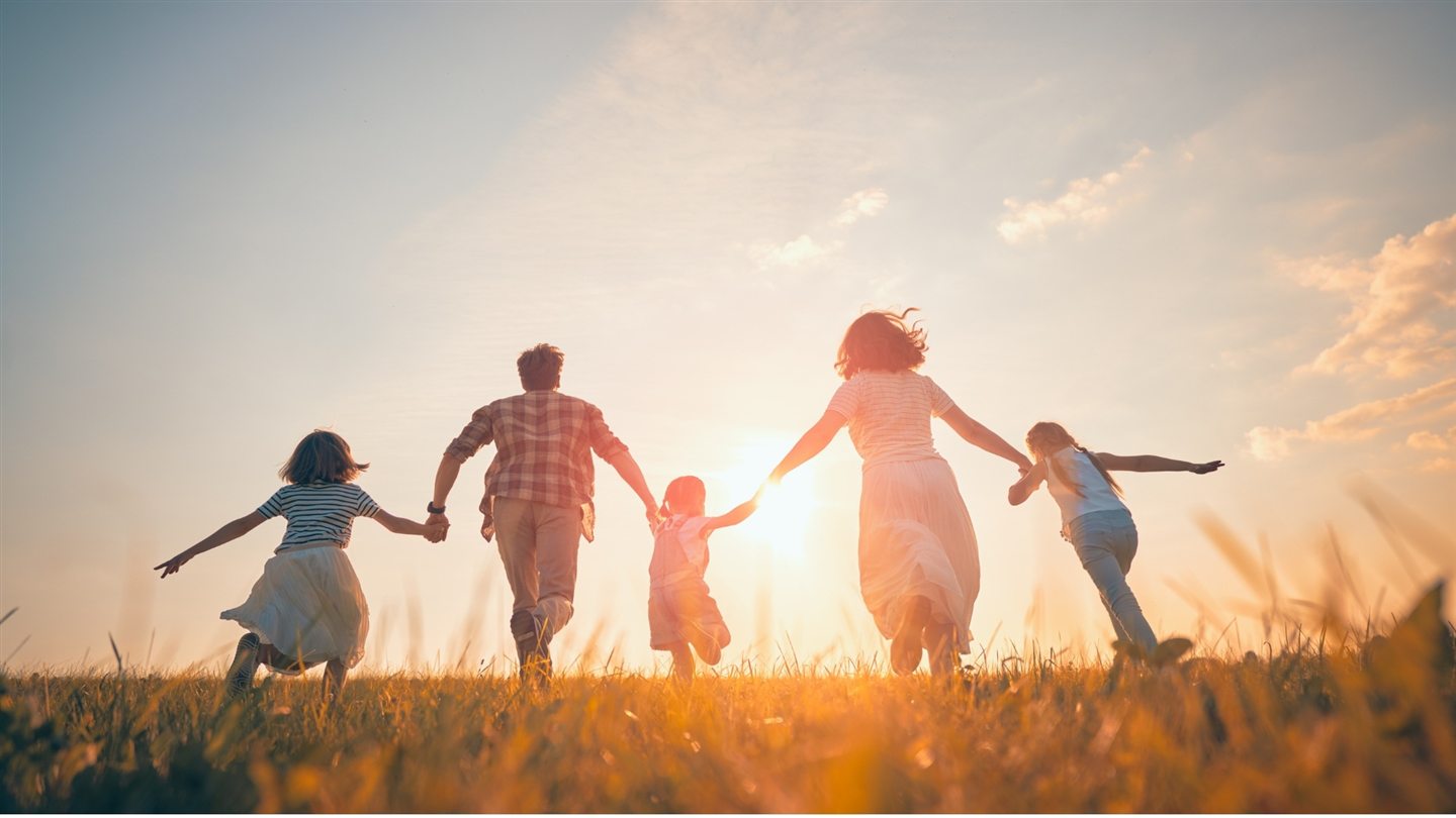 Family running hand in hand in a field at sunset