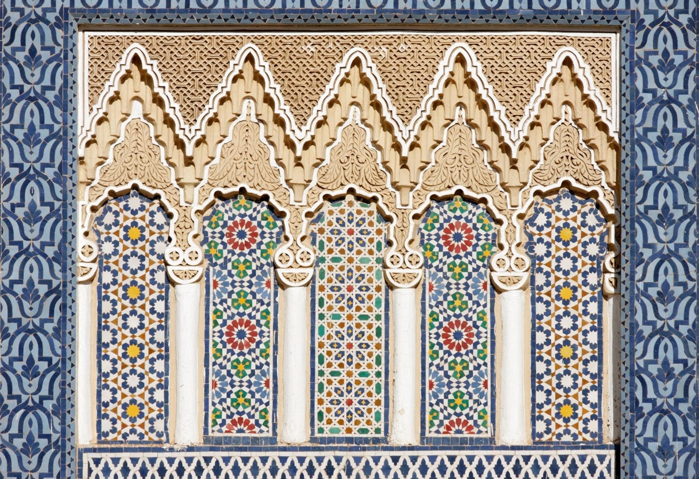 Lace-like carved plaster arches above zellige columns