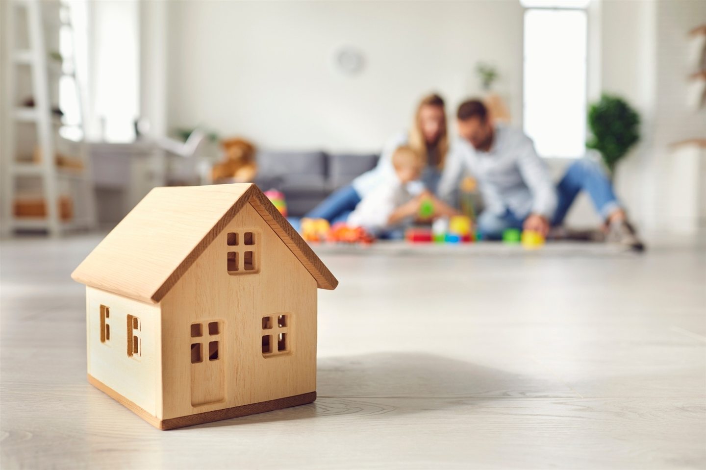 Wooden model house in the foreground, family playing in the living room