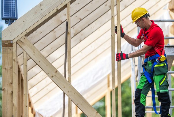 Carpenter in a harness raising a wood frame