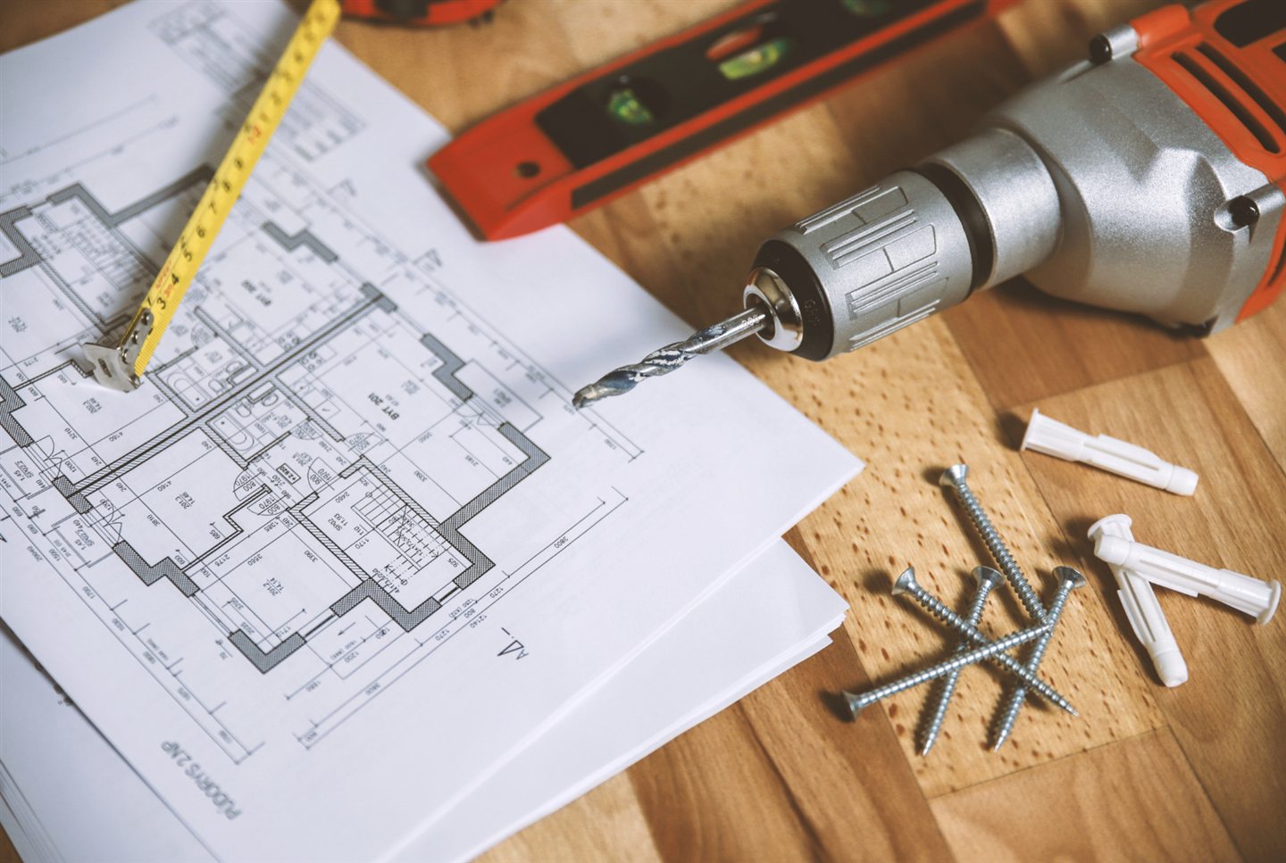 Plans de maison, ruban à mesurer, niveau et perceuse sur une table de bois