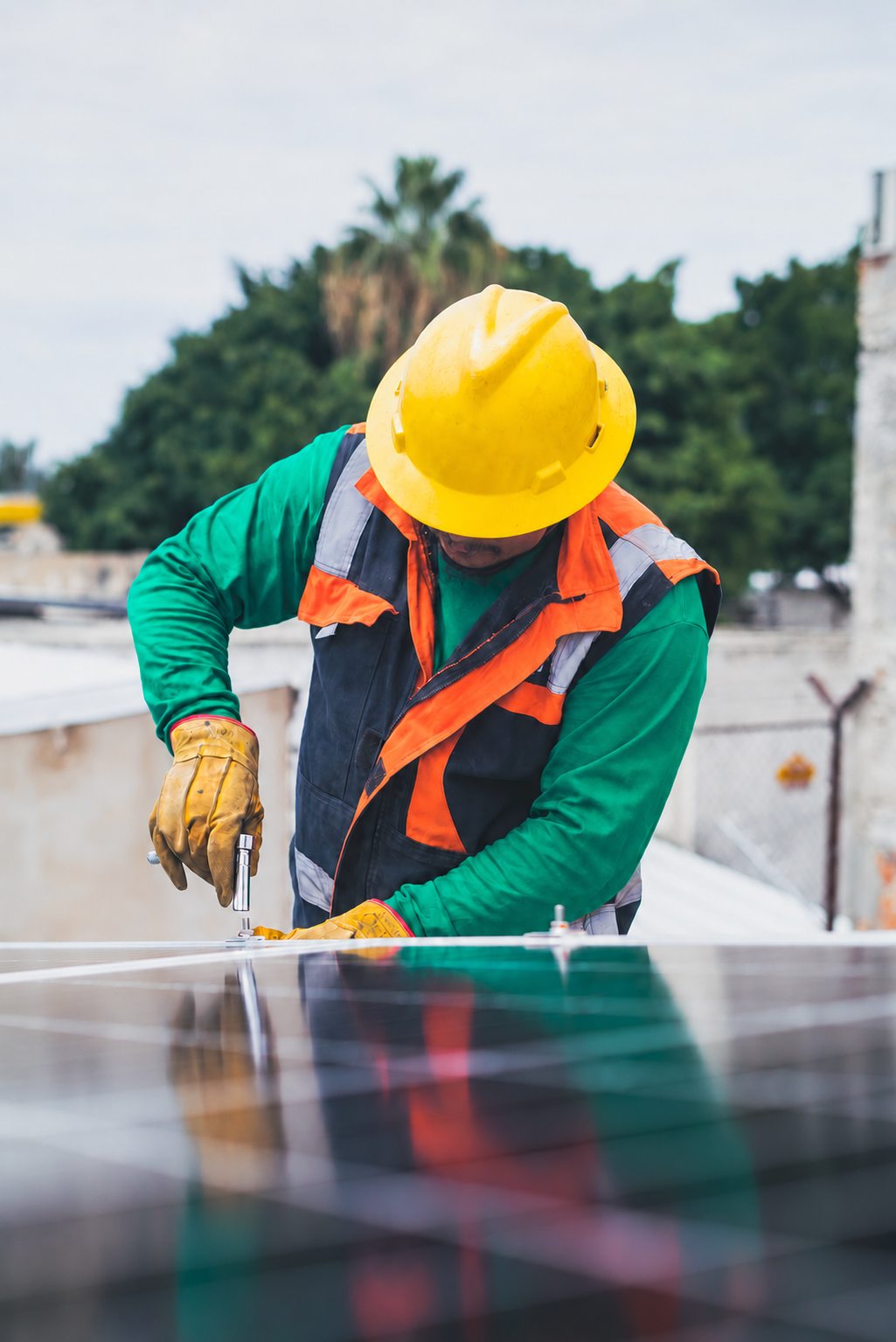 Installer in a yellow hard hat fastening a solar panel on a roof