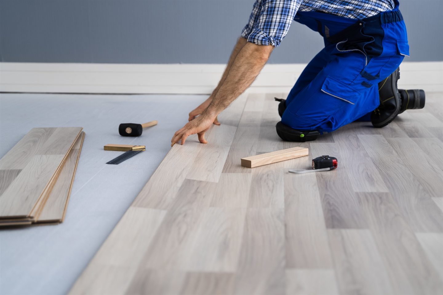 Artisan à genoux qui pose des lattes de plancher flottant
