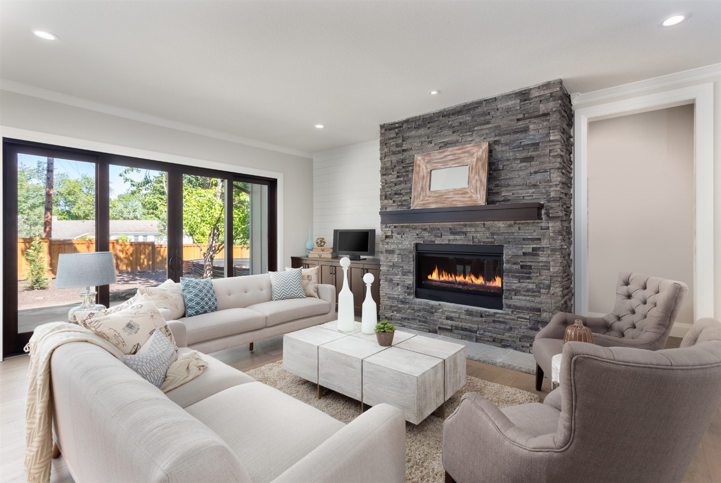 White living room open to the yard, fireplace set in a grey stone wall