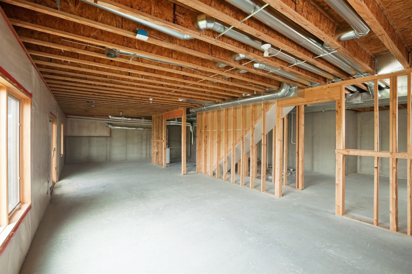 Sous-sol brut avec ossature de bois, conduits de ventilation au plafond et dalle de béton