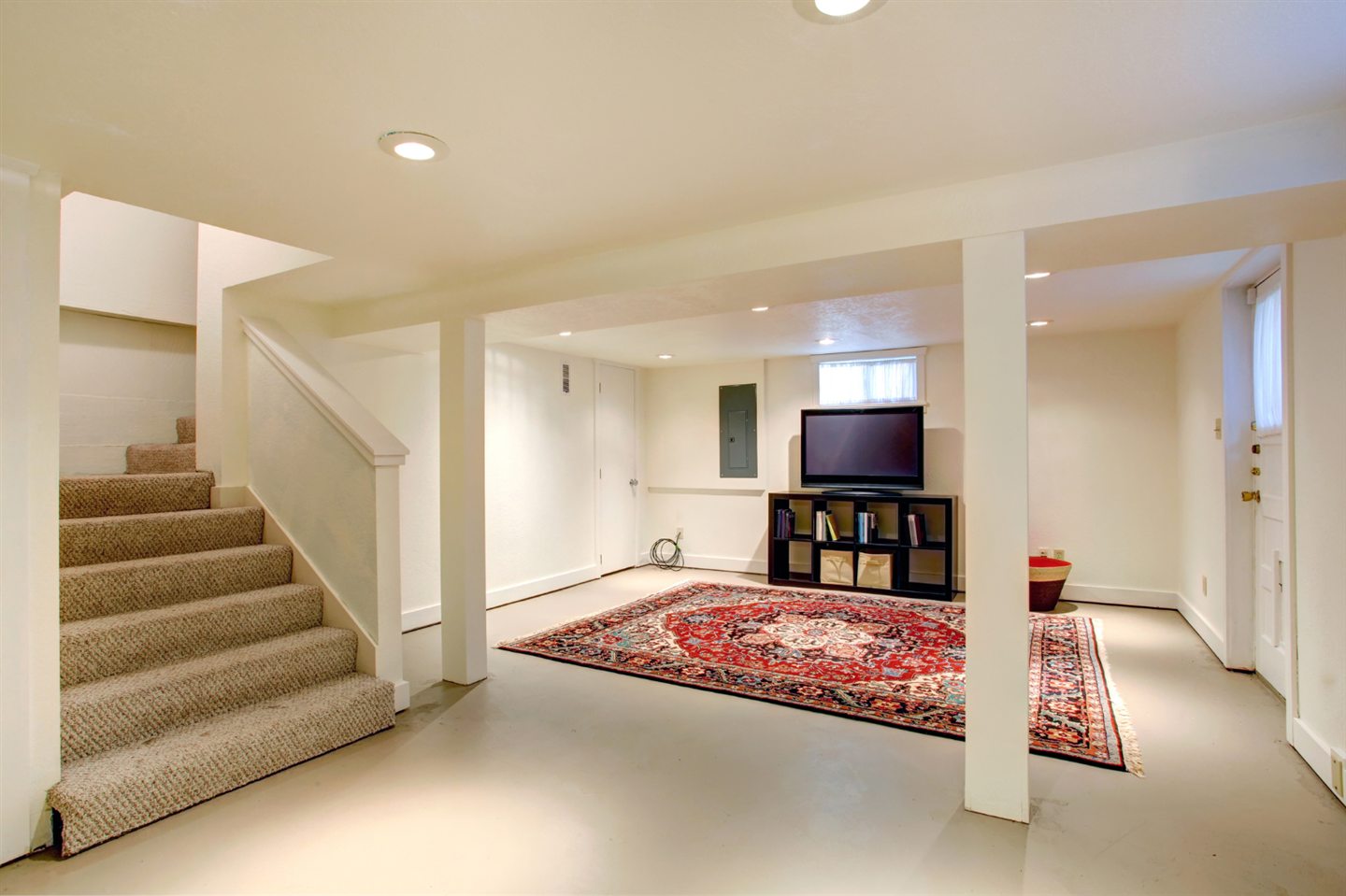 Sous-sol fini et lumineux, tapis oriental, meuble télé et escalier recouvert de moquette