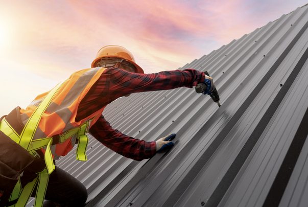 Roofer fastening metal roofing at sunset